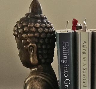 'Falling' & 'Aging' books in Buddha bookends beside her couch. In front is a sign, 'Peace is every breath'