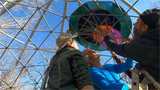 Heather, Hubbs, JSun and others installing "Triangulation" the first panel up on the dome frame.